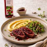 Plated dish of venison steak with mashed potatoes and greens with a balsamic cherry vinegar dressing.