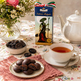 Tea set with a cup of tea, chocolate covered prunes, and a box of Stuhmer Szilvas Betyar on a floral tablecloth.