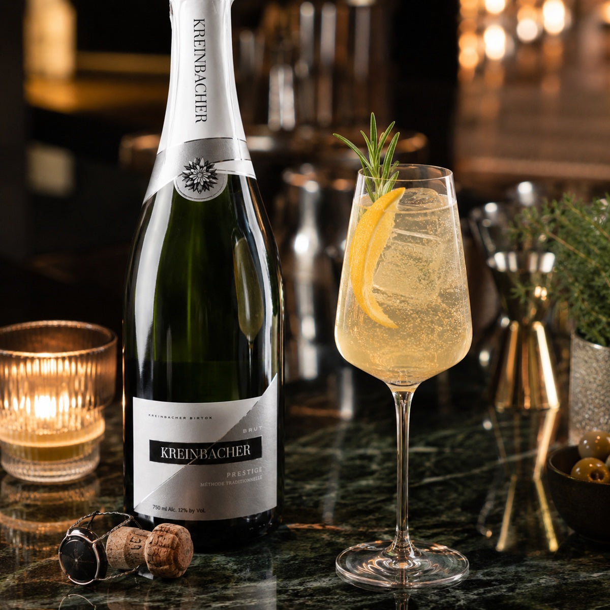Bottle of Kreinbacher sparkling wine with a glass of champagne cocktail on a bar counter.