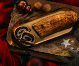 A cozonac unguresc poppy seed roll on a gold tray with Christmas ornaments and a red fabric background