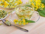 Clear glass cup filled with primrose tea on a wooden surface, with cowslip flowers in the background.