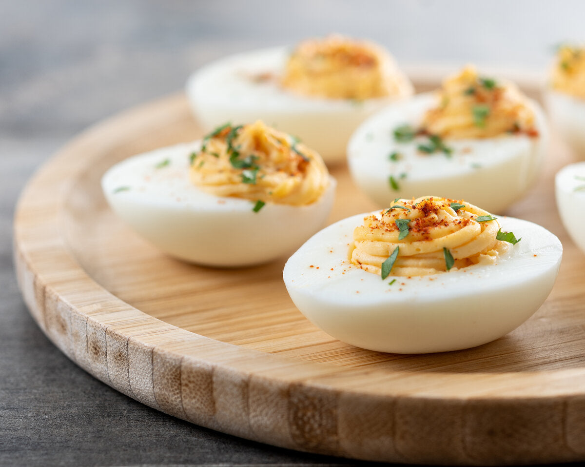 Devilled eggs on a wooden cutting board with a sprinkling of paprika and dried lovage leaves.