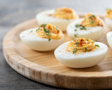 Devilled eggs on a wooden cutting board with a sprinkling of paprika and dried lovage leaves.