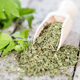 Dried lovage in a wooden scoop with fresh leaves on a wooden surface.