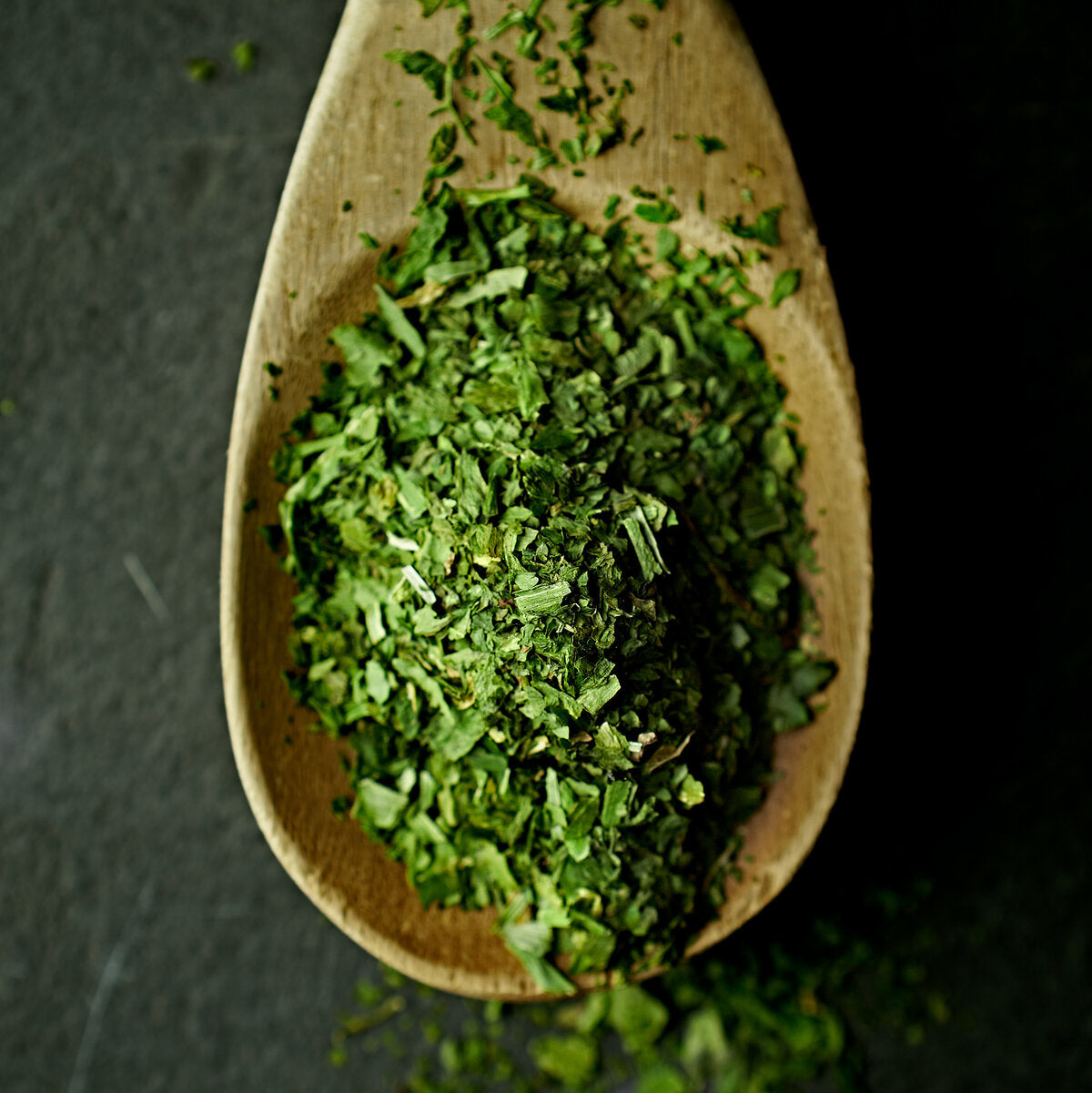 Wooden spoon filled with wild garlic made from dried ramsons leaves, on a dark background.