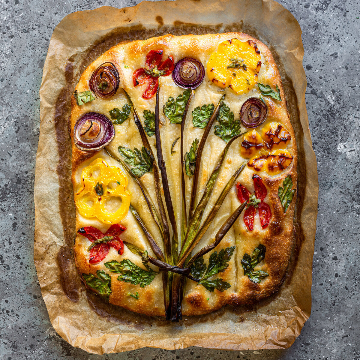 Freshly baked focaccia bread on parchment paper with vegetables and summer savory.