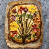 Freshly baked focaccia bread on parchment paper with vegetables and summer savory.