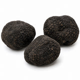 Three whole fresh black truffles of the summer truffle variety, arranged on a clean white background.