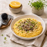 A bowl of creamy risotto with freshly grated whole black truffle and microgreens on top.