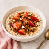 Bowl of healthy porridge with strawberries, nuts and grape skin powder on a light surface.
