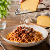 Person grating caraway cheese over a bowl of spaghetti on a wooden table.