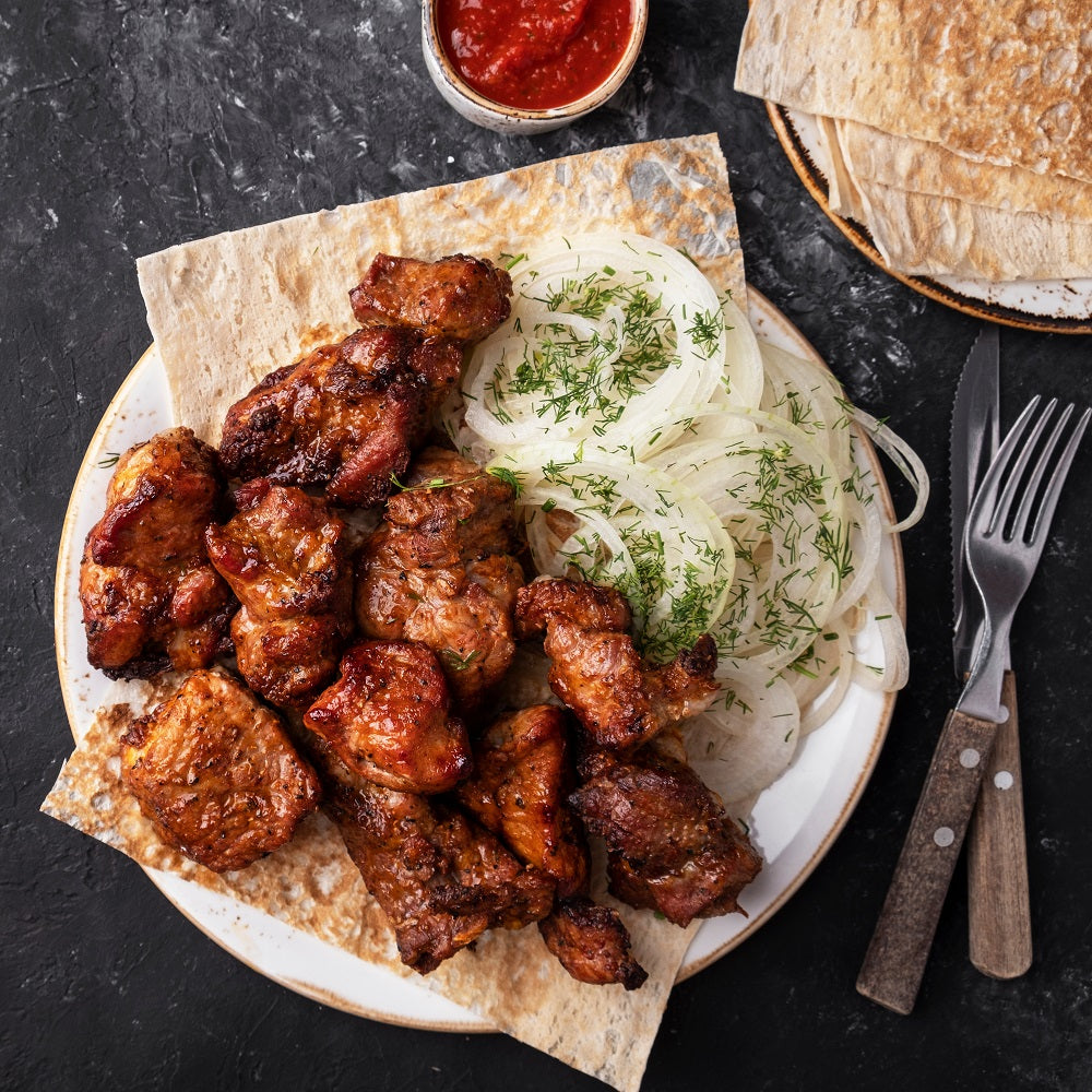 Plated dish of grilled meat with onions, pita bread and BBQ ketchup.