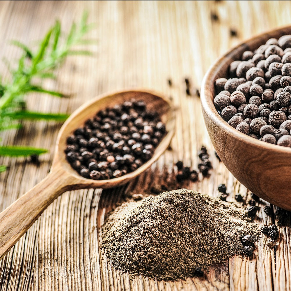 Black pepper in a bowl and on a wooden spoon with a pile of ground black pepper on a rustic wooden surface.