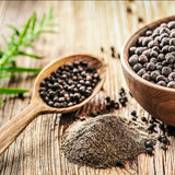 Black pepper in a bowl and on a wooden spoon with a pile of ground black pepper on a rustic wooden surface.