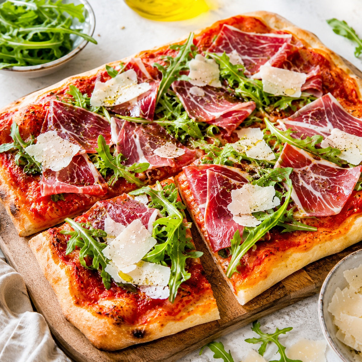 Pizza with mangalitsa ham, rocket, and parmesan on a wooden board.