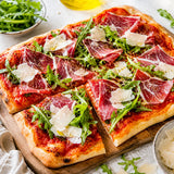 Pizza with mangalitsa ham, rocket, and parmesan on a wooden board.