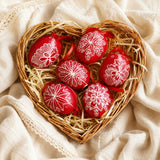 Heart-shaped wicket basket with six hand-made red Easter eggs on a textile background.