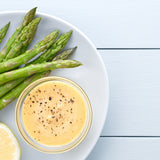 Green asparagus on a white plate with a bowl of Hollandaise sauce sprinkled with ground black pepper.