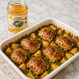 Baked dish with honey-mustard-marinated chicken thighs, potatoes, and peas next to a jar of acacia honey.