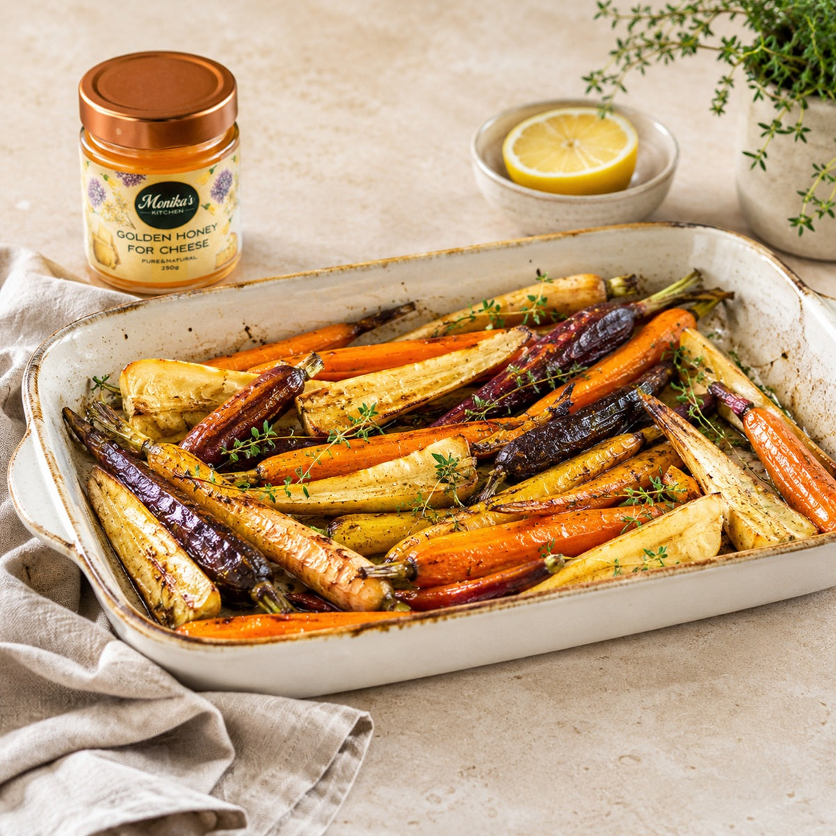 Dish of honey roasted rainbow carrots and parsnips with a jar of golden honey, herbs and lemon.