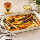Dish of honey roasted rainbow carrots and parsnips with a jar of golden honey, herbs and lemon.