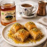 Baklava with honey on a plate with organic mountain honey and a cup of coffee in the background.