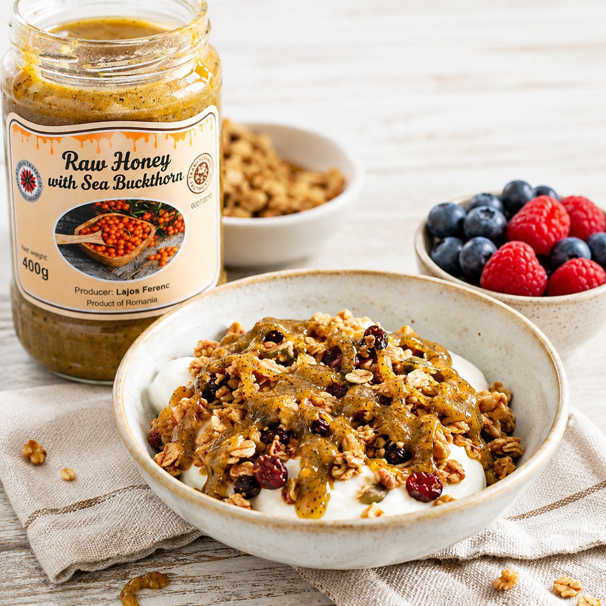 Bowl of granola with yogurt, jar of raw honey with sea buckthorn, and berries on a wooden surface.