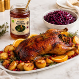 Roasted duck with potatoes, oranges, and red cabbage on a white plate with a jar of organic pine honey.