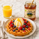 Waffles with ice cream and berries on a plate with a jar of organic mountain honey.