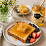 Toast with honey, honeycomb, berries, and a jar of Monika's Acacia Honey with Honeycomb on a table.