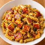 Dish of hot honey halloumi pasta with fusilli pasta, halloumi cubes, drizzled with hot honey.