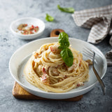 Plate of pasta Carbonara with Iberico bacon and garnished with basil.