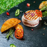 Meat wrapped in smoked Iberico bacon with roast potato wedges on dark slate.