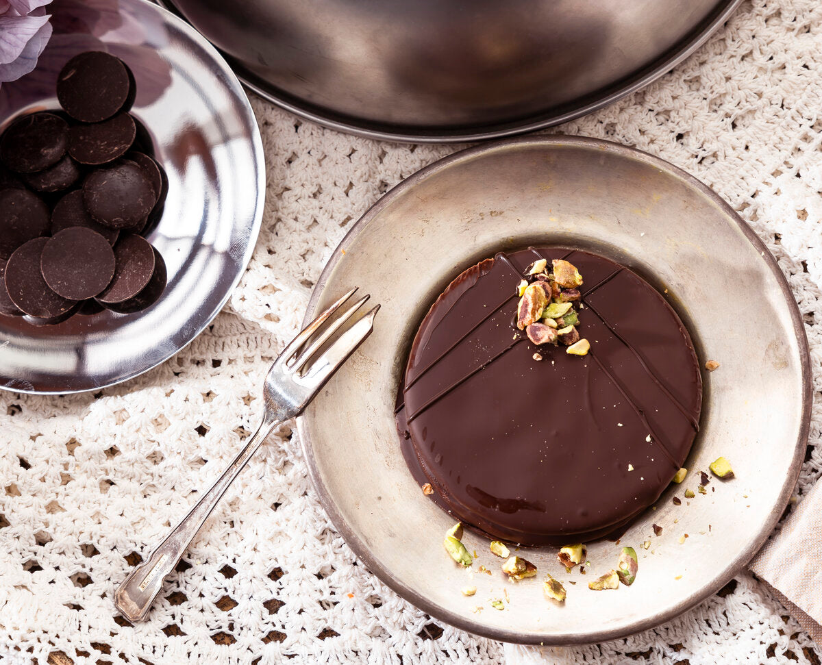 An ischler chocolate cookie with pistachios on a plate with chocolate coins and a fork.