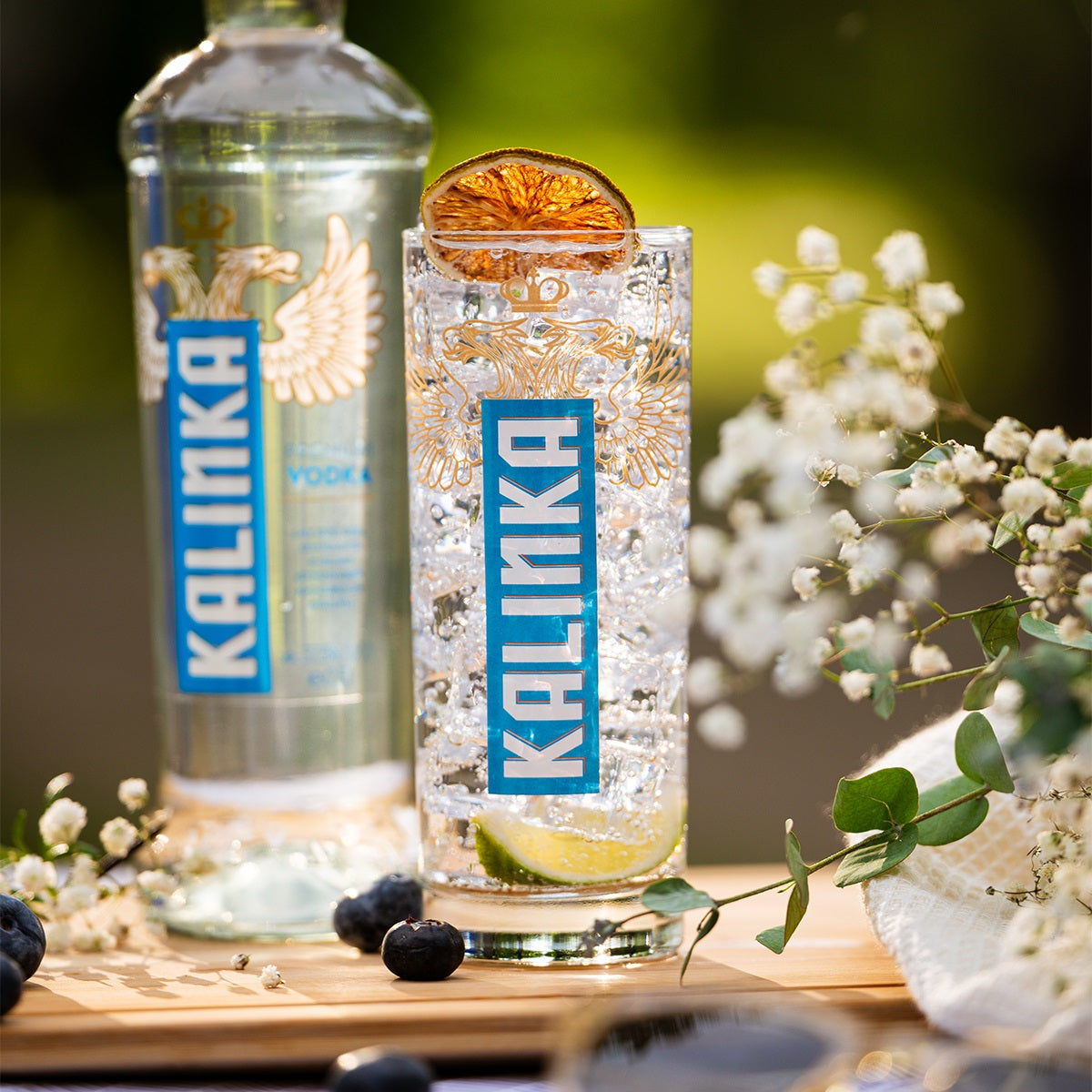 Glass of Kalinka vodka with a cocktail garnish on a wooden surface with flowers in the background