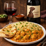 Plate of curry with naan bread and a bottle of wine with a labrador dog label in the background.
