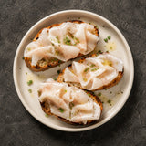 Three slices of toasted bread with slices of lardo and green herbs on a white plate against a dark background.