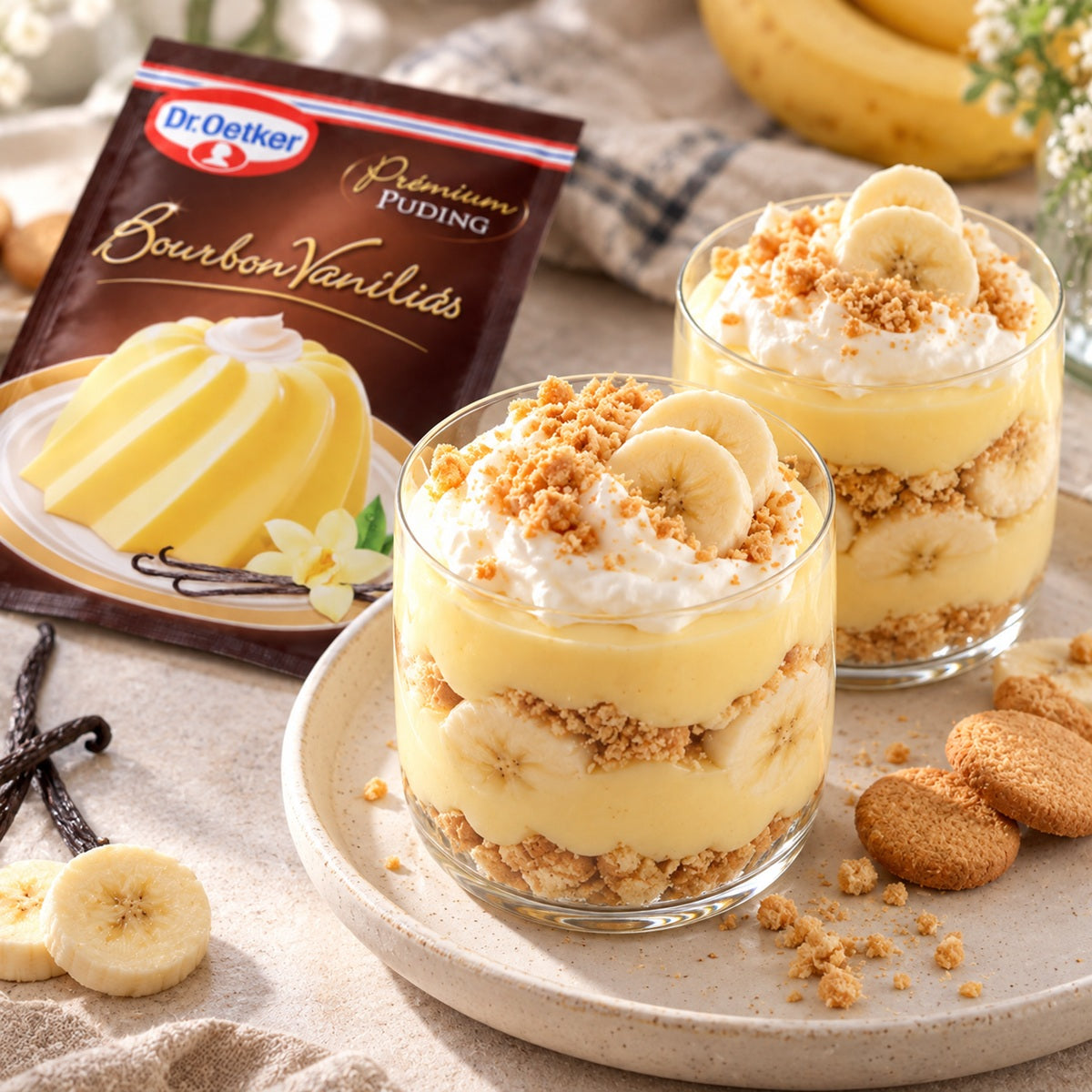 Two glasses of Dr Oetker Bourbon Vanilla Pudding dessert topped with banana slices and crumbled cookie crumbs.