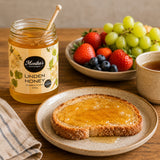 Jar of Monika's Linden Honey with toast and fruit on a wooden table