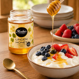 Bowl of yoghurt with berries and honey being drizzled, Monika's Kitchen Linden Honey jar in the background.