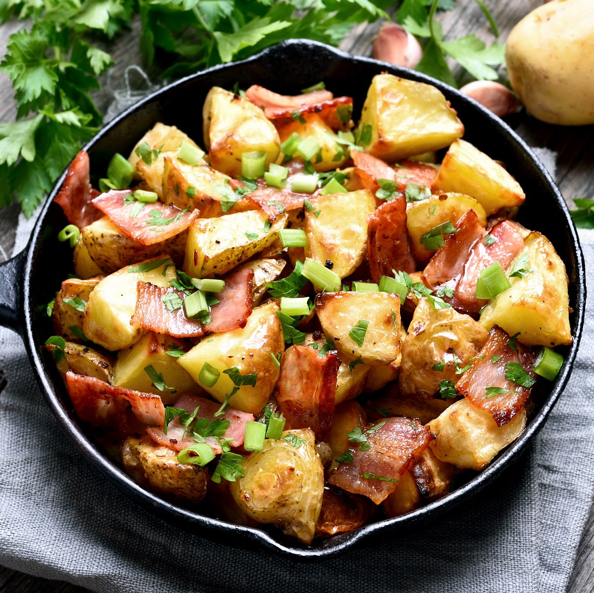 Roast potatoes loaded with bacon, cheese and green onions in a black skillet on a grey surface.