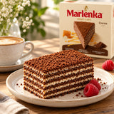 A slice of layered Marlenka Cocoa Honey Cake with cocoa dusting on a ceramic plate, garnished with fresh raspberries. 