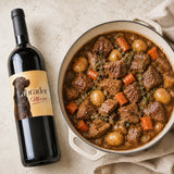 Bottle of Labrador Merlot wine next to a pot of slow-cooked beef bourguignon stew.