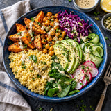 A top-down view of a blue ceramic bowl filled with a colourful salad of vegetables and cooked millet grain.