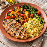 A plated meal featuring sliced grilled chicken breast, cooked yellow millet grains and roasted vegetables.