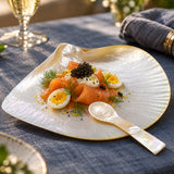 A close-up of a gourmet salmon salad served on a mother-of-pearl shell-shaped plate with a small spoon.