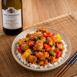 Plate of Chinese orange chicken with a bottle of orange wine on a wooden table.