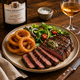 Steak with onion rings and salad on a plate with a bottle of orange wine and glass in the background.