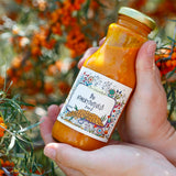 Hand holding a bottle of organic sea buckthorn juice with a blurred background of sea buckthorn berries.