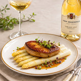 A plated dish of white asparagus and pan-fried foie gras with microgreens, set on a beige tablecloth beside a glass of Tokaji dessert wine.